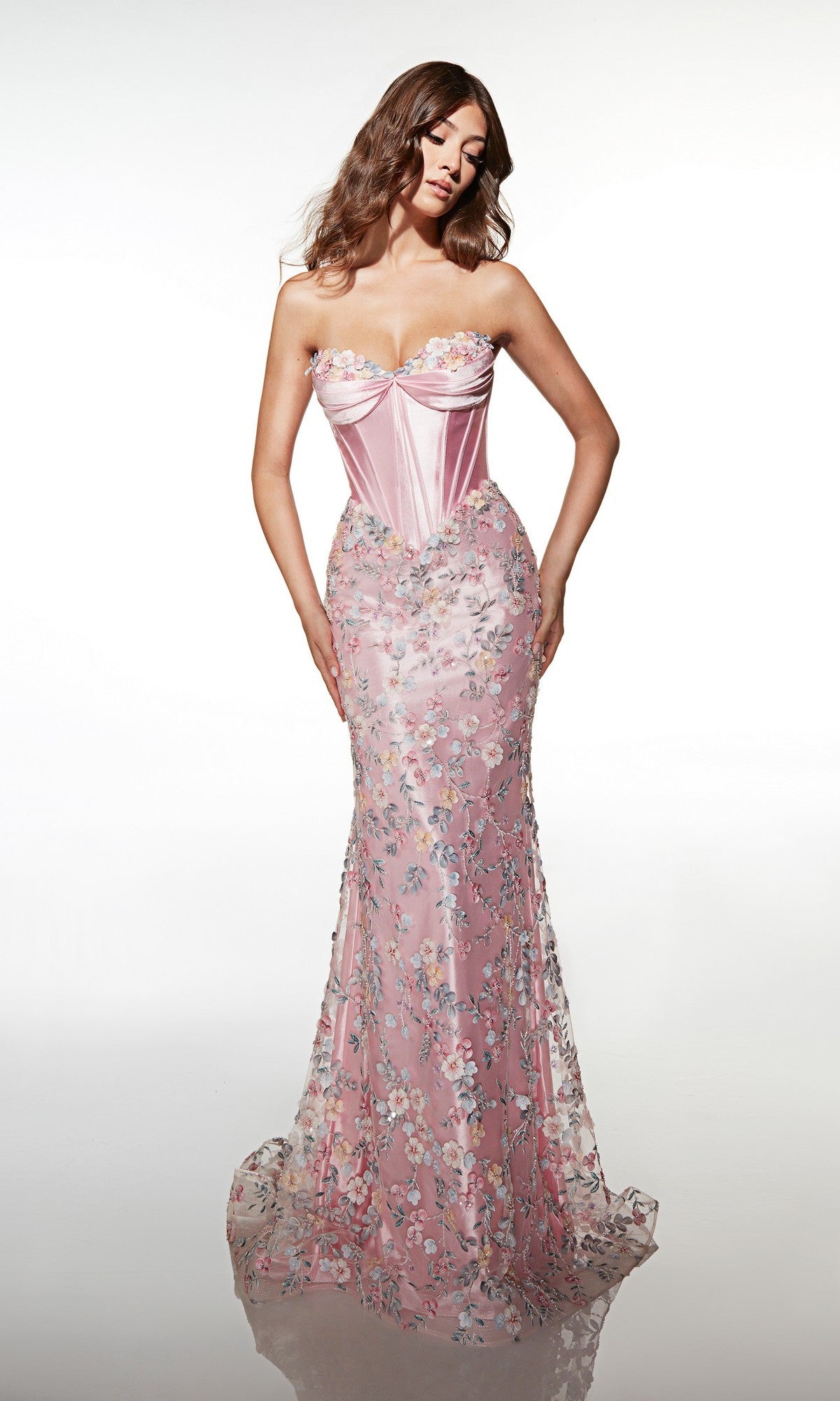Wearing the Alyce 62197 Long Prom Dress, a woman stands against a white background in a strapless pink gown with a corset bodice and a sheer skirt decorated with 3D floral embellishments and intricate floral patterns.